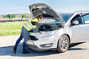 Woman testing car battery in broken car on roadside