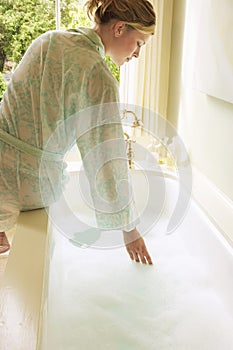 Woman Testing Water In Bathtub Filled With Bubbles