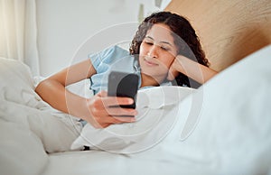 Woman texting, checking messages and holding phone while reading sms and lying awake in her bed in the morning. Happy