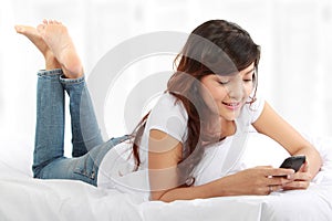 Woman texting on phone lying on bed