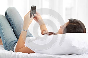 Woman texting on phone lying on bed