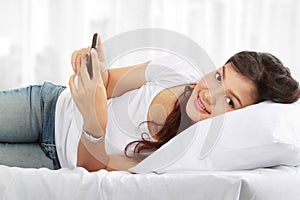 Woman texting on phone lying on bed