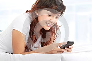 Woman texting on phone lying on bed