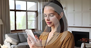 Woman texting sms use cellphone standing in cozy living room