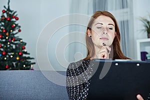 Woman think about christmas wih list on sofa