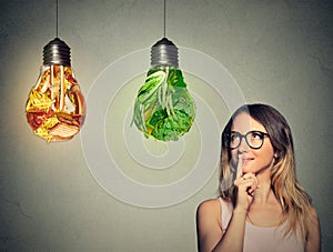 Una mujer pensamiento buscando arriba sobre el basura comida a verde verduras conformado cómo la luz bombilla 