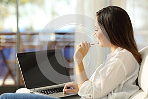 Woman thinking using a laptop with blank screen