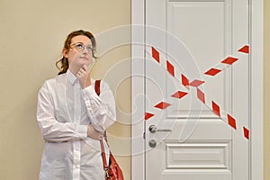 A woman in thought in front of a closed office door. The concept of problems with the work and closure of companies due to