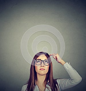 Woman with thoughtful expression looking up on gray wall background