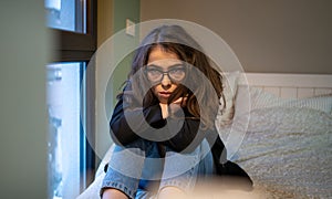 Woman in thoughtful solitude sits by window with serene expression in softly lit room