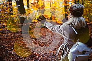 Woman throwing autumn leaves into the air. Carefree, happiness concept. Scenic fall park