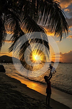Woman throwing a baby in the air at sunset, Hillsborough Bay, Carriacou Island, Grenada
