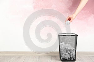 Woman throwing crumpled paper ball into basket near pink wall, closeup. Space for text