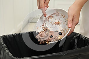 Woman throwing oatmeal with berries into bin indoors, closeup