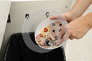 Woman throwing oatmeal with berries into bin indoors, closeup