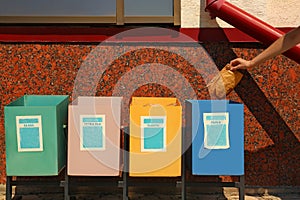 Woman throwing paper into recycling bin outdoors