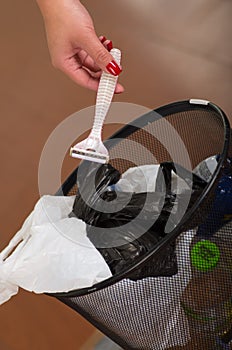 Woman throwing a shaver inside of the garbage, on wooden background