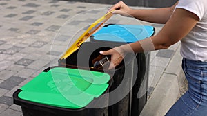 Woman throwing two empty plastic water bottle in recycling bin. Tree recycling bins outdoors