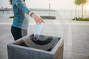 Woman throwing a used surgical face mask in the trash outdoors