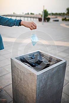 Woman throwing a used surgical face mask in the trash outdoors