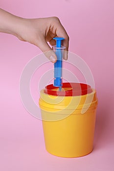 Woman throwing used syringe into sharps container  on pink background, closeup