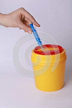 Woman throwing used syringe into sharps container on white background, closeup