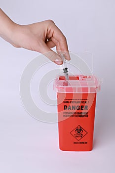 Woman throwing used syringe into sharps container on white background, closeup