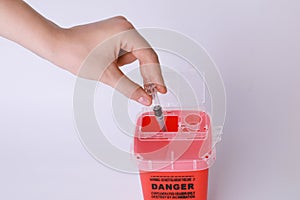 Woman throwing used syringe into sharps container on white, closeup