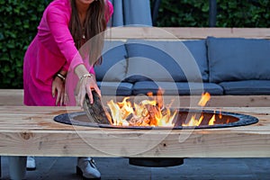 Woman throws logs on fire pit in the garden on a summer day