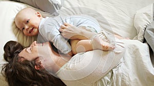 Woman tickling and hugging her year-old son. Sunny family morning mom and baby in bed. Mothers Day