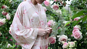 Woman tie belt of peignoir in garden among blooming roses