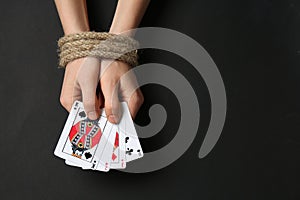 Woman with tied hands and playing cards on dark background. Concept of addiction