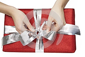 Woman ties a ribbon of a red gift box on white background