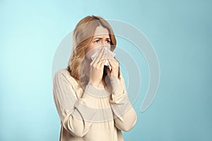 Woman with tissue suffering from runny nose on light blue background. Space for text