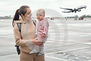 Woman and toddler girl stand against taking-off airliner