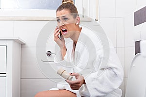 Woman on toilet complaining via phone about lack of paper