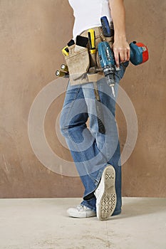 Woman With Toolbelt And Drill Leaning Against Wall