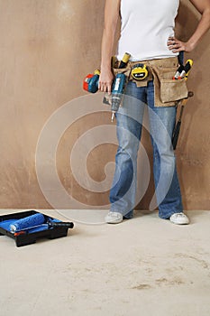 Woman With Toolbelt And Drill Leaning Against Wall photo