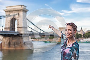 Woman with toothy smile pointing to Chain Bridge at Budapest, Hungary