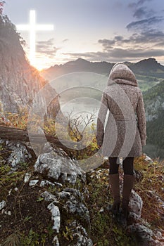 Woman on top of the mountain looking at the Christian Cross