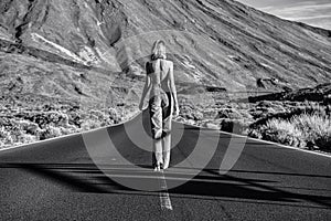 Woman topless traveler in jeans walking away on the street over the wild mountains landscape. Back view. Feminist