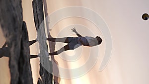 Woman tosses ball high up and catches it in the sky at sunset by the sea.