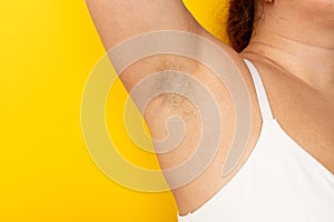 Woman touch hairy underarms with hand closeup, free copy space, yellow background. Raised arm with armpit hair. Female
