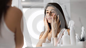 Woman Touching Face Looking At Skin In Mirror At Bathroom