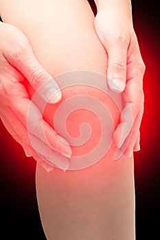 Woman touching her knee at pain point, with red spot on knee,  on black. Joint pain, Arthritis and tendon problems.