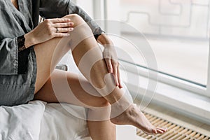 Woman touching her legs in bedroom, closeup