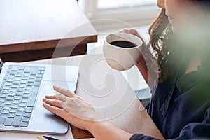 A woman touching on laptop touchpad while drinking coffee and working in office