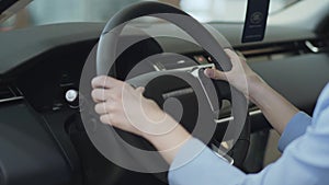 Woman touching steering wheel with her fingers close up. Modern girl examining automobile in motor show. Concept of