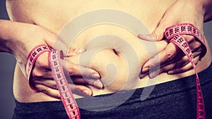 Woman touching stomach holding measuring tape