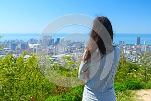 Woman tourist admiring cityscape of Batumi city from mountain in sunny day.